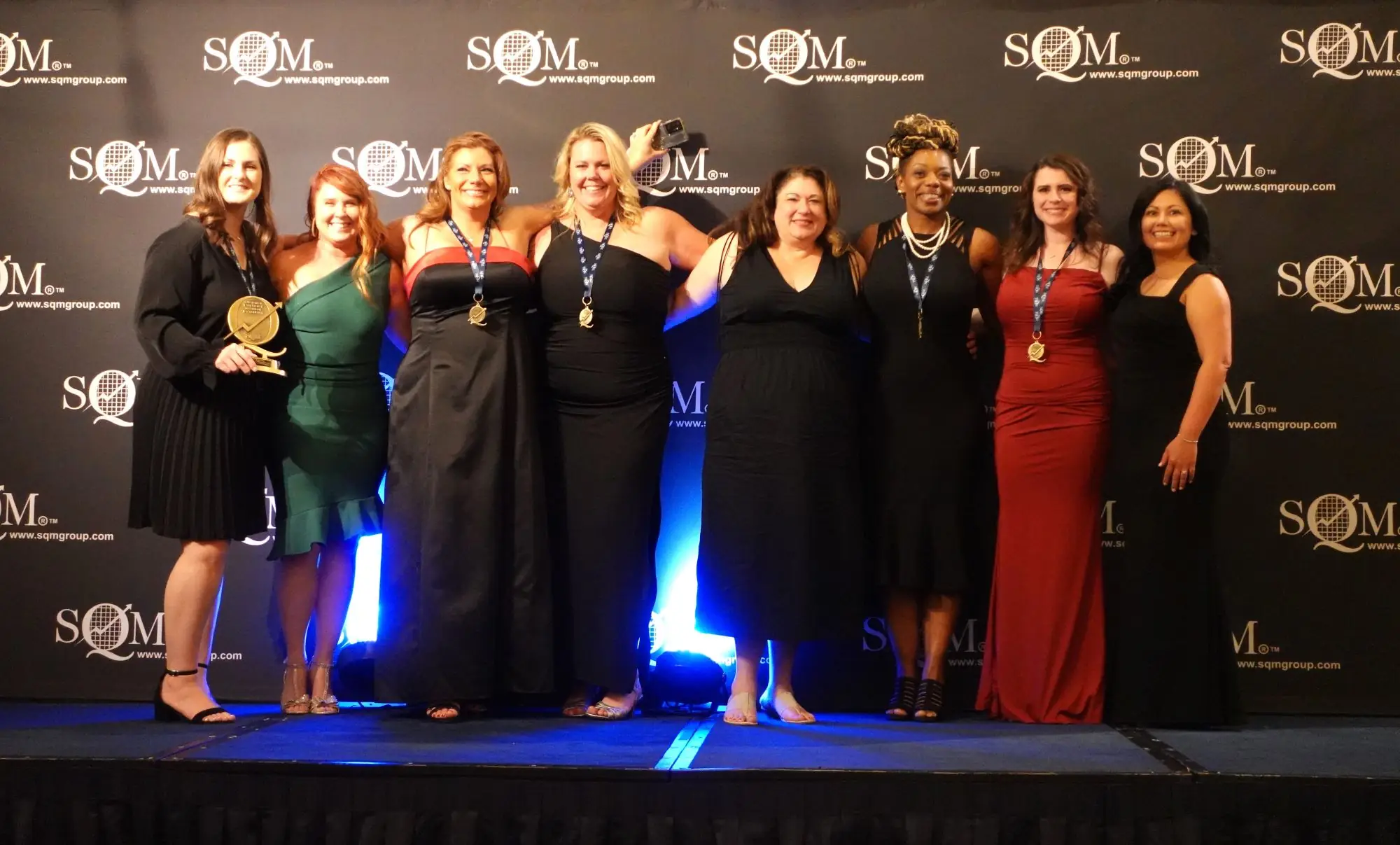 six women standing on a stage holding an award and wearing award medallions