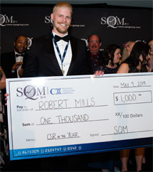 A man with a big smile, who is wearing a tuxedo, holding an over-sized prize money cheque for $1,000.